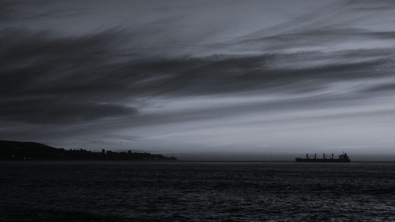 A cargo vessel on the horizon at dusk off a coastline