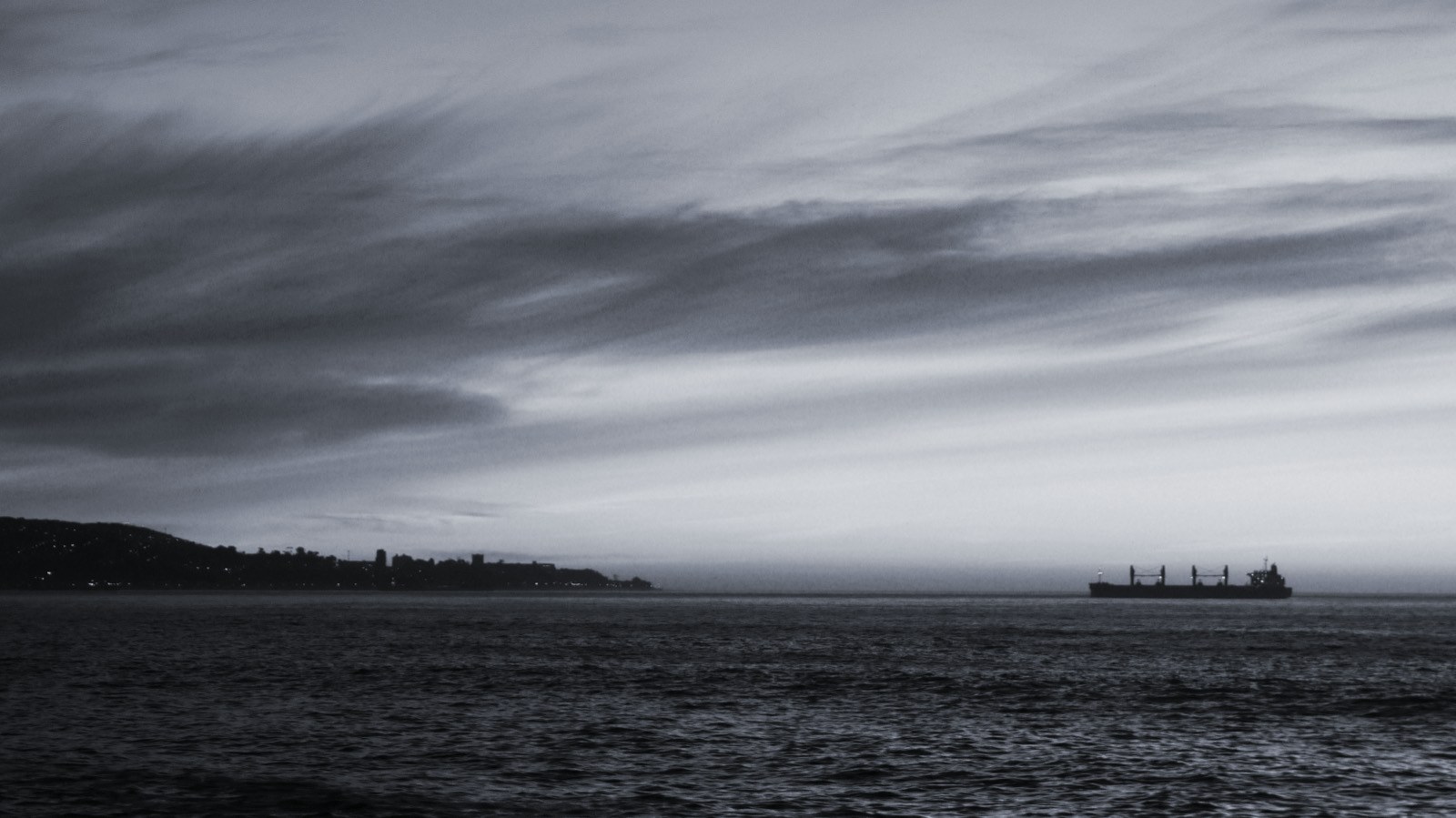 A cargo vessel at anchor on the horizon at dusk